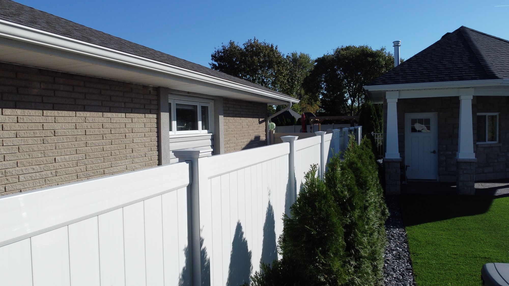 White Homeland Vinyl fence that we installed in Tecumseh. With a row of cedar plants in front of it, the contrasting colours sharply accentuate this craftsman style home.